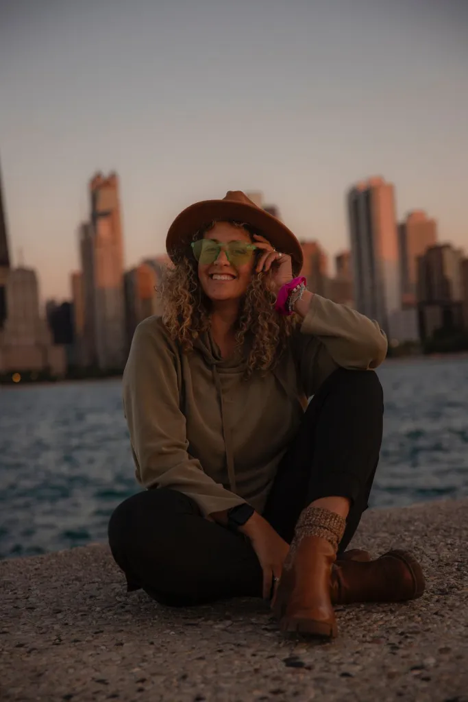 Rabbi Tori Greene sitting on a city lakefront at sunset, skyline behind her