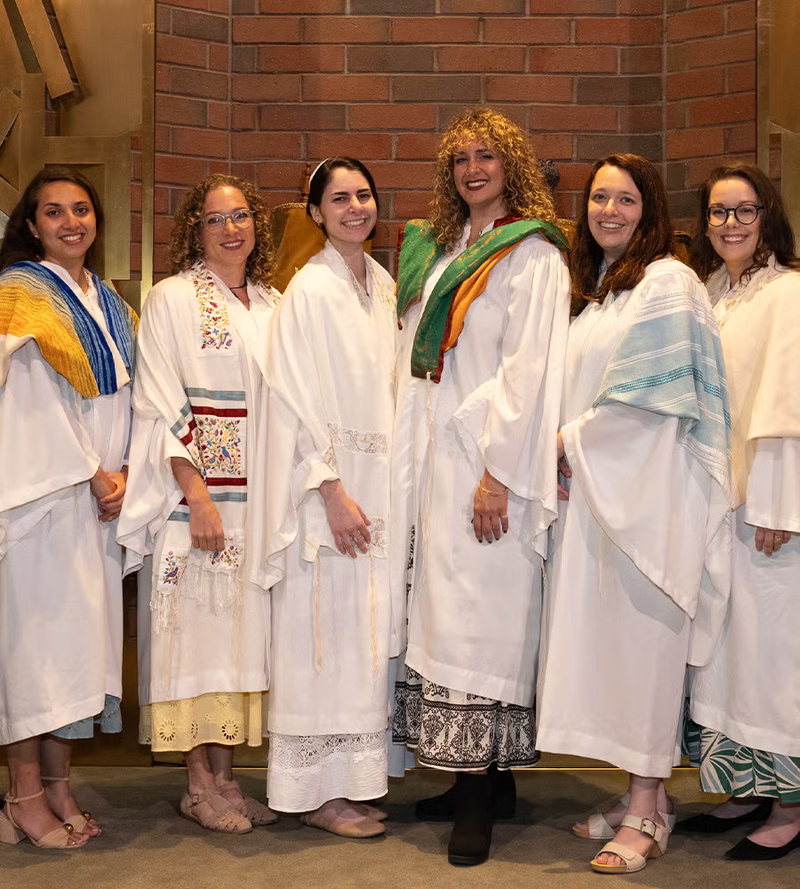 Six newly ordained rabbis in white robes at Stephen Wise Temple in Los Angeles, Tori Greene fourth from left in a green and orange tallit